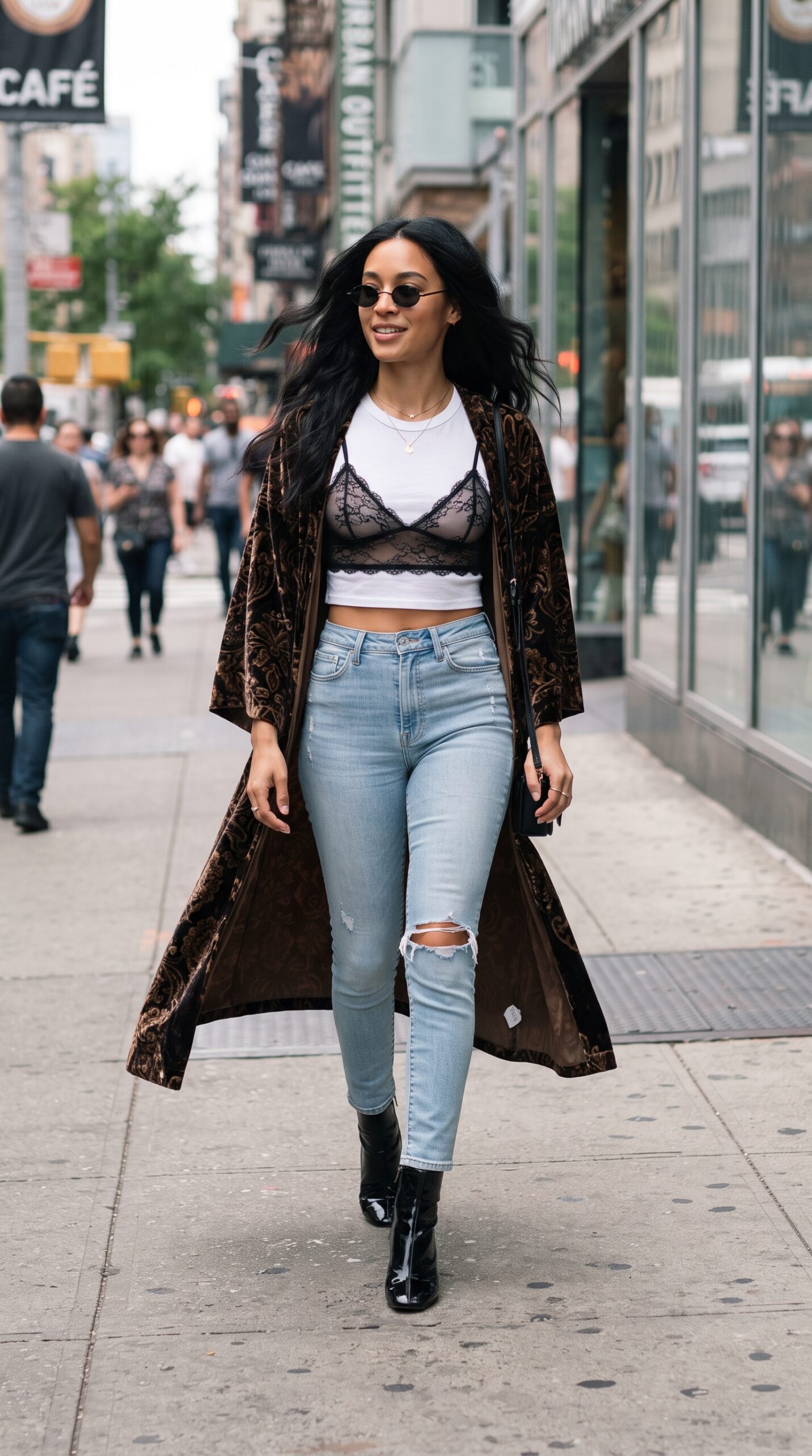 Donna che cammina in città indossando una bralette in pizzo nero sopra una t-shirt bianca corta, jeans chiari strappati e un lungo kimono in velluto marrone.