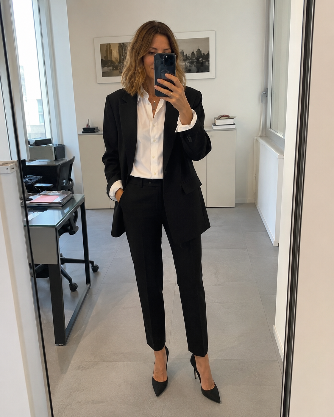 Donna di circa 40 anni con pantaloni a sigaretta neri, camicia bianca e blazer oversize in ufficio