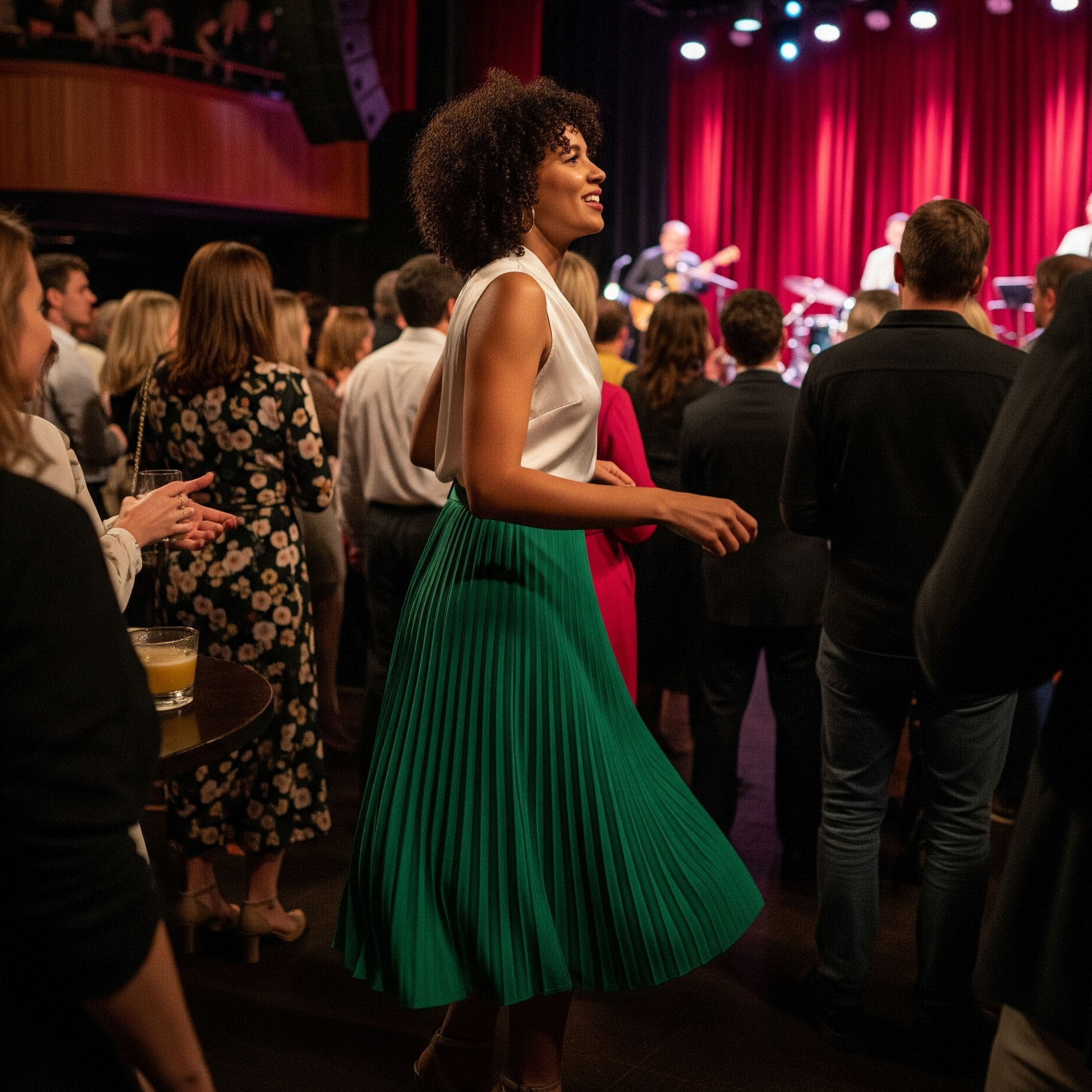 Spettatrice con capelli ricci indossa un look per un concerto jazz: una gonna midi plissettata verde e un top di seta bianco, mentre si gode la musica.
