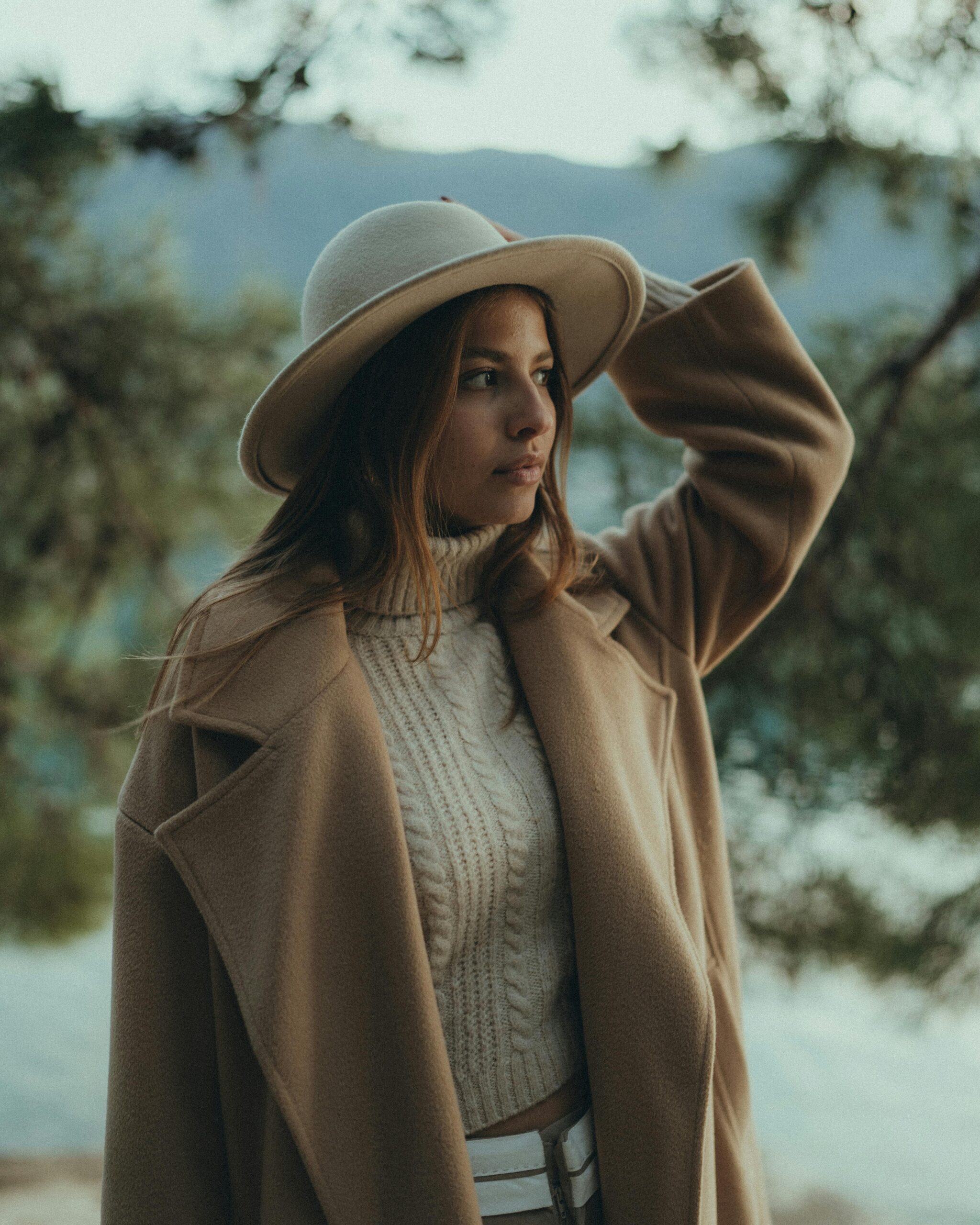 Donna con cappotto in lana beige, maglione a trecce e cappello chiaro in un outfit invernale elegante all'aperto