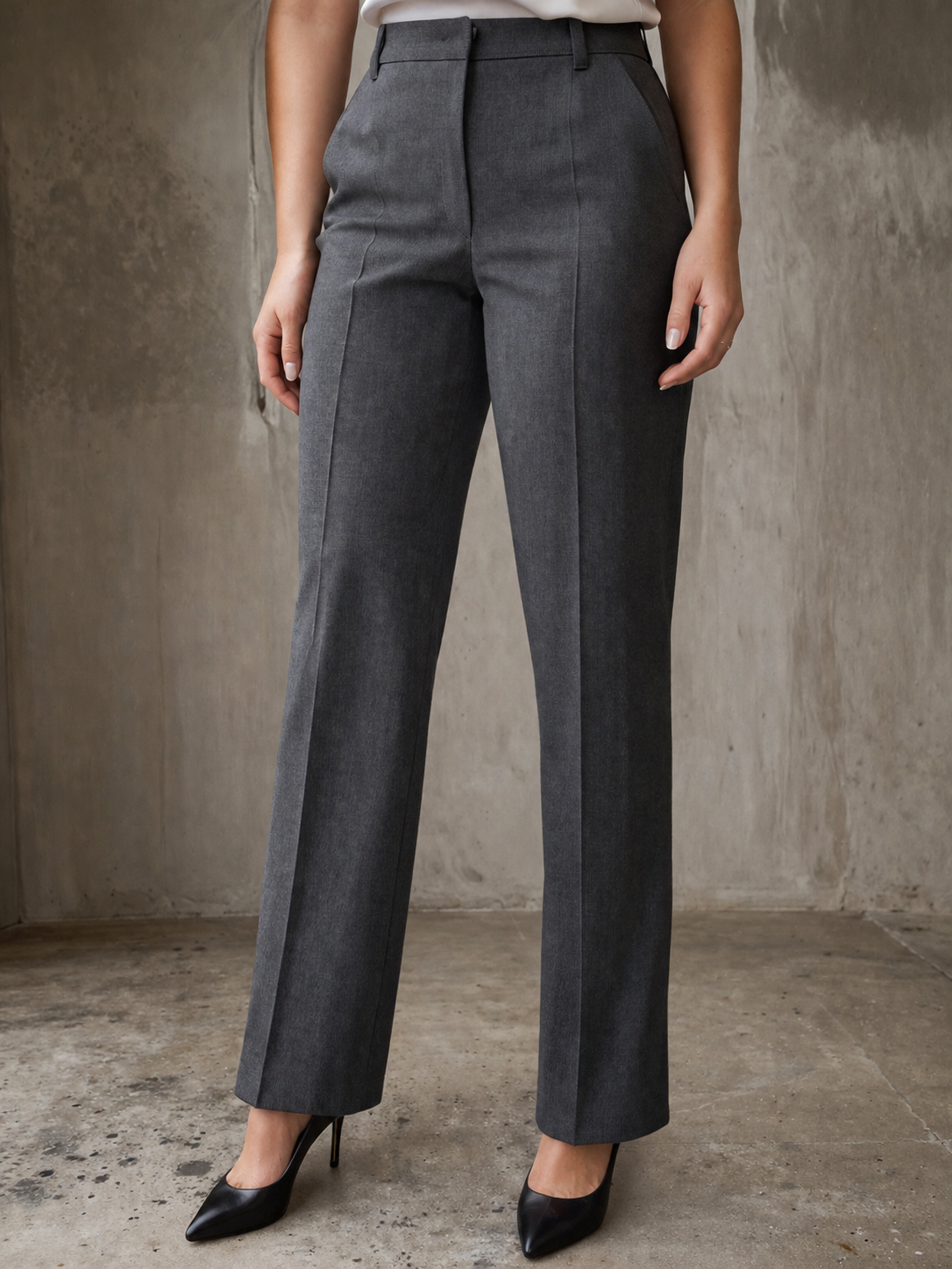 Donna che indossa pantaloni grigi a vita alta con taglio dritto e piega centrale, abbinati a decolleté nere a punta per allungare la silhouette delle gambe.