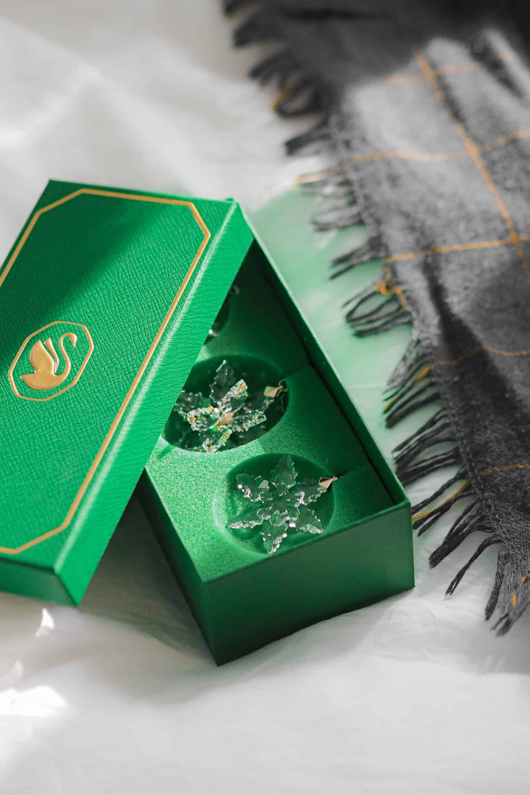 L'iconica scatola regalo verde Swarovski aperta rivela la brillantezza di due gioielli in cristallo a forma di fiocco di neve, simbolo della qualità e della magia del brand.