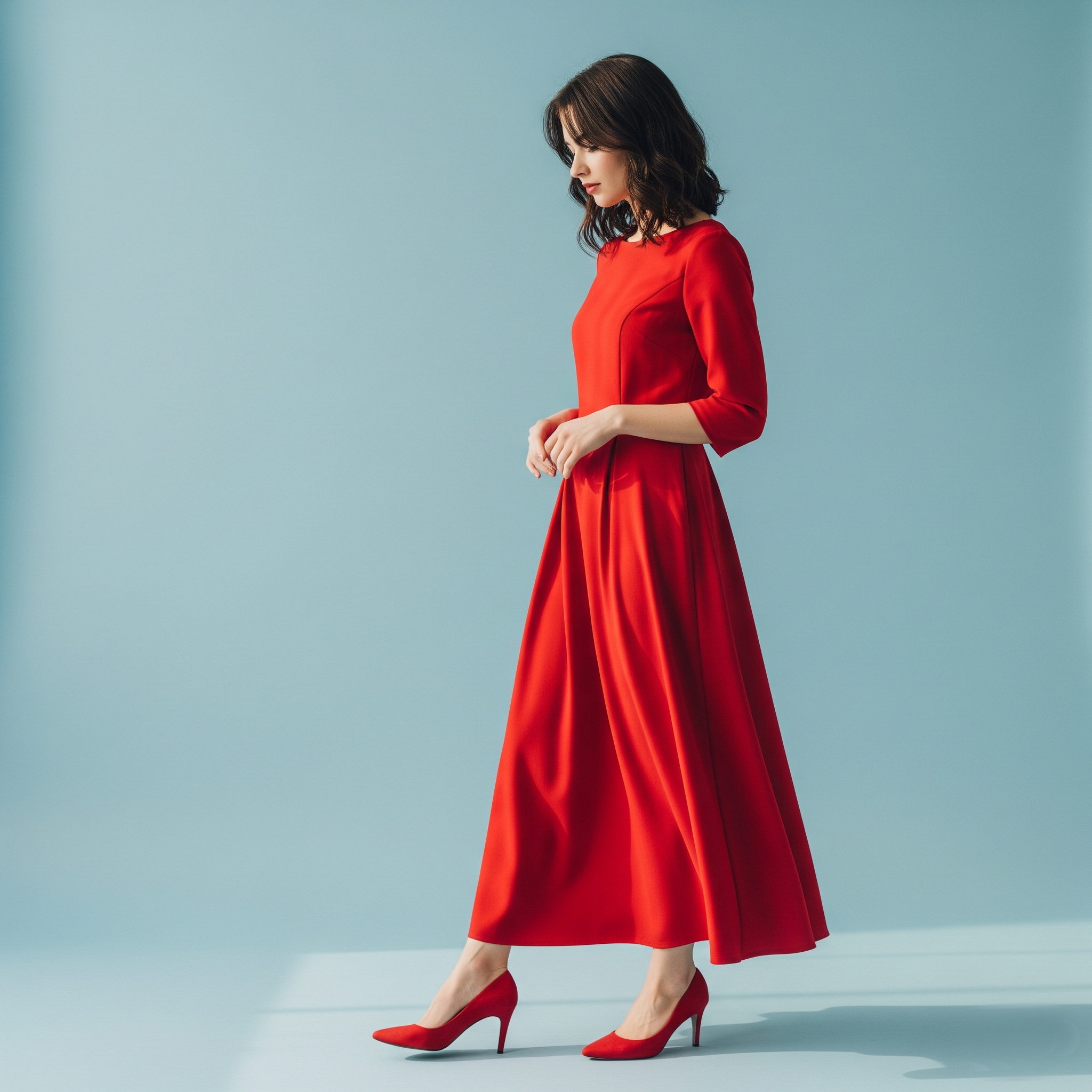 Donna in posa di profilo indossa un look monocromatico con vestito rosso lungo e décolleté rosse abbinate.

