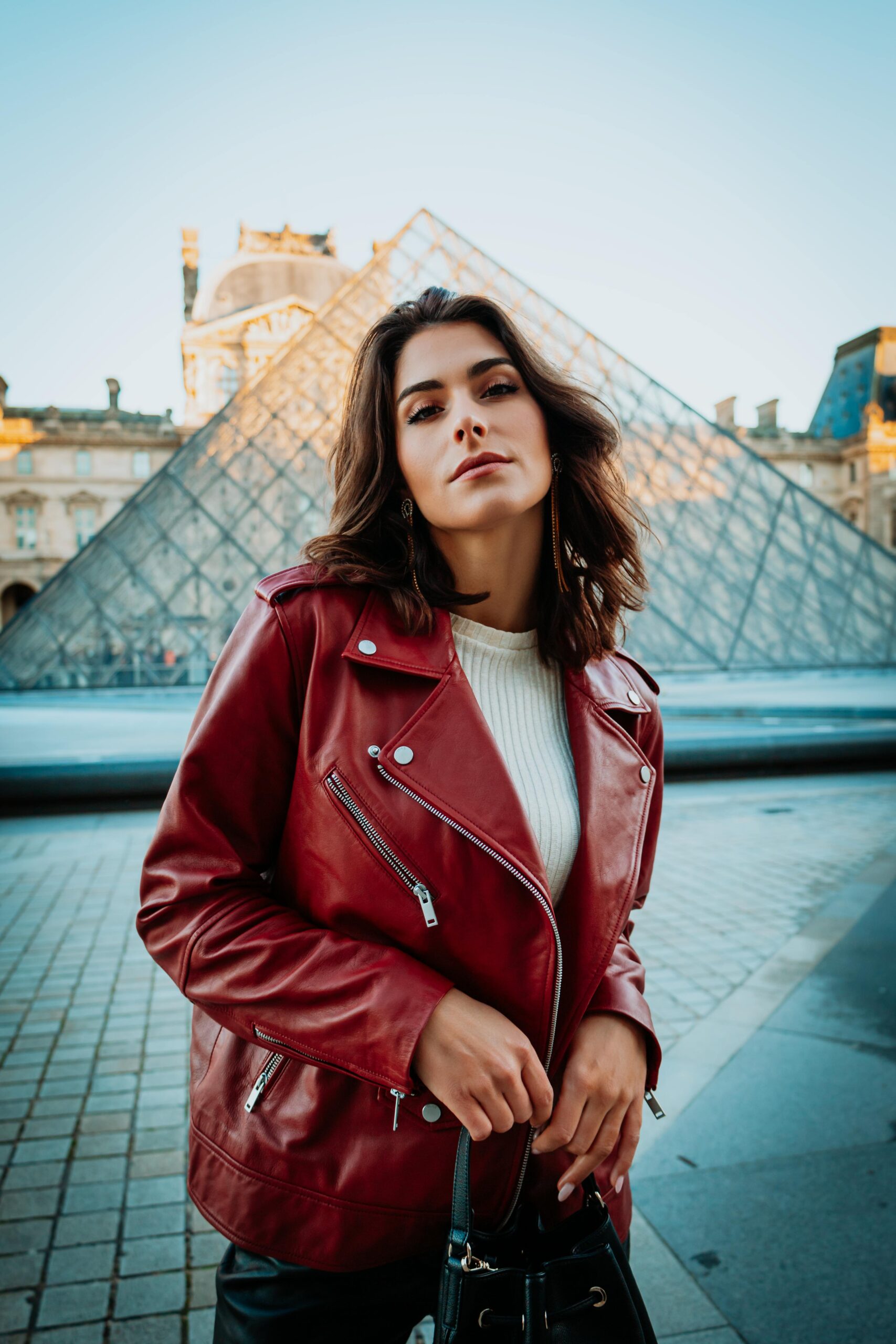 Donna con giacca in finta pelle rossa e maglione bianco davanti al Louvre, simbolo di stile e versatilità autunnale.