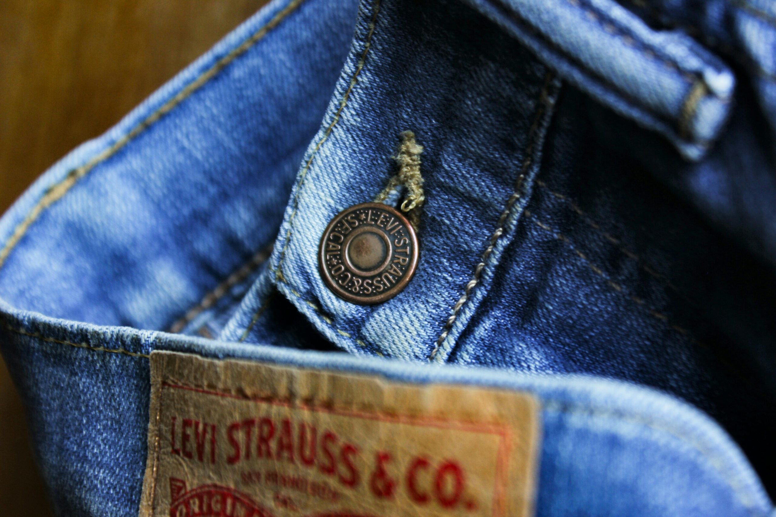 Dettaglio ravvicinato di un jeans Levi's blu con il bottone metallico e l'etichetta in pelle "Levi Strauss & Co." in primo piano. Ideale per articoli su guida acquisto e modelli Levi's uomo.