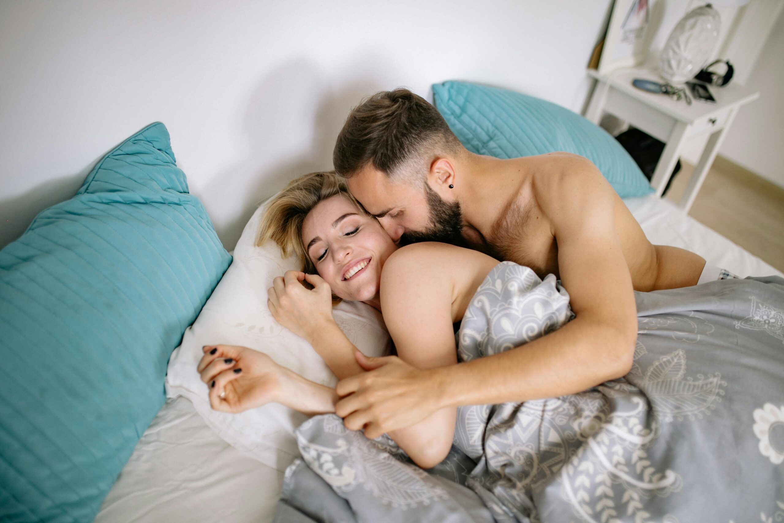Frasi Hot e Dirty Talk: Cosa Dire a un Uomo Durante il Sesso 2 Coppia a letto che si abbraccia e ride, momento intimo e sensuale ispirazione per frasi hot da dire a un uomo
