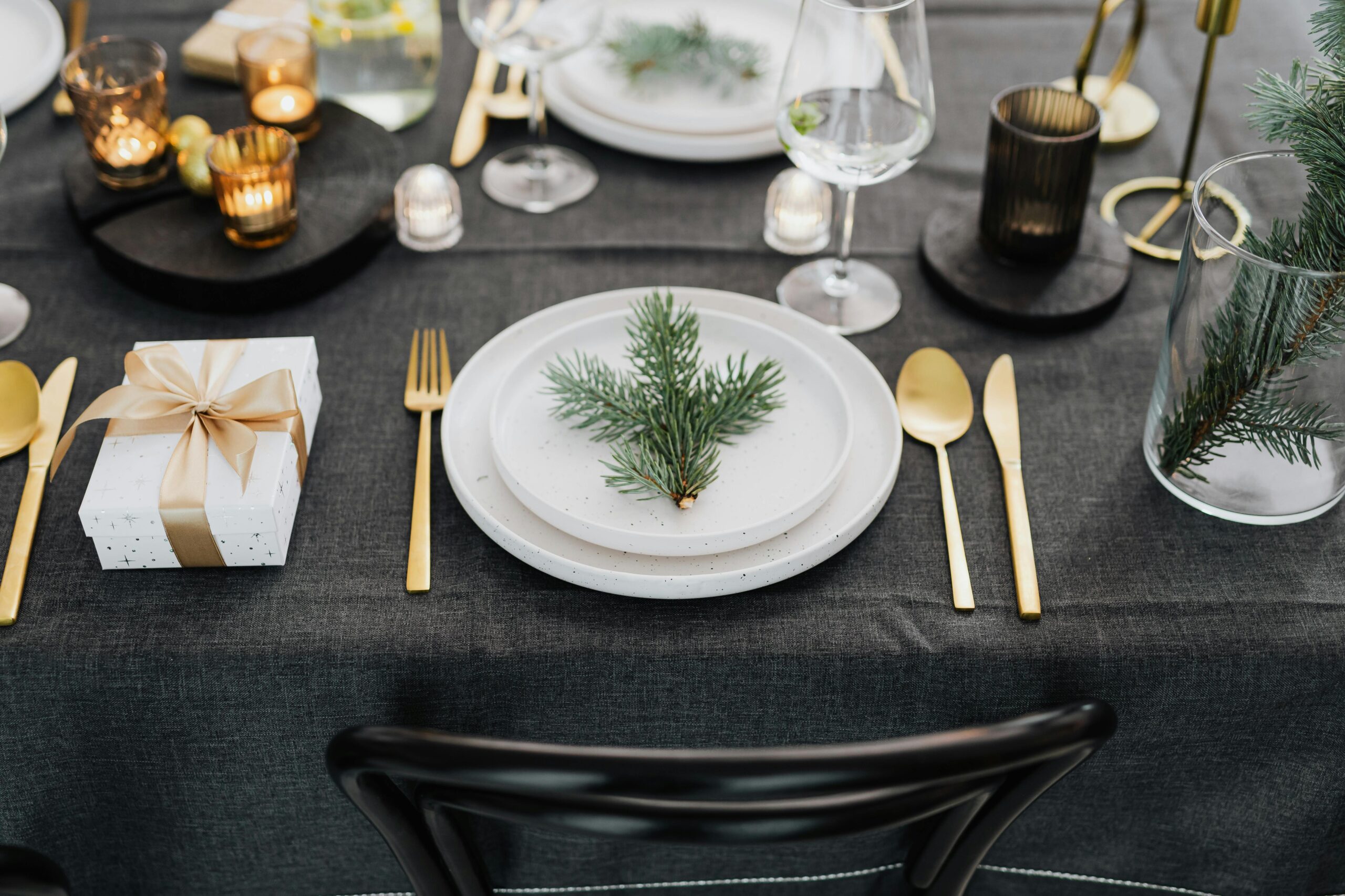 Tendenze Colori Natale 2025: 6 decorazioni casa da copiare 5 Tavola di Natale elegante con tovaglia nero opaco, posate oro e decorazioni verdi, stile moderno trend 2025