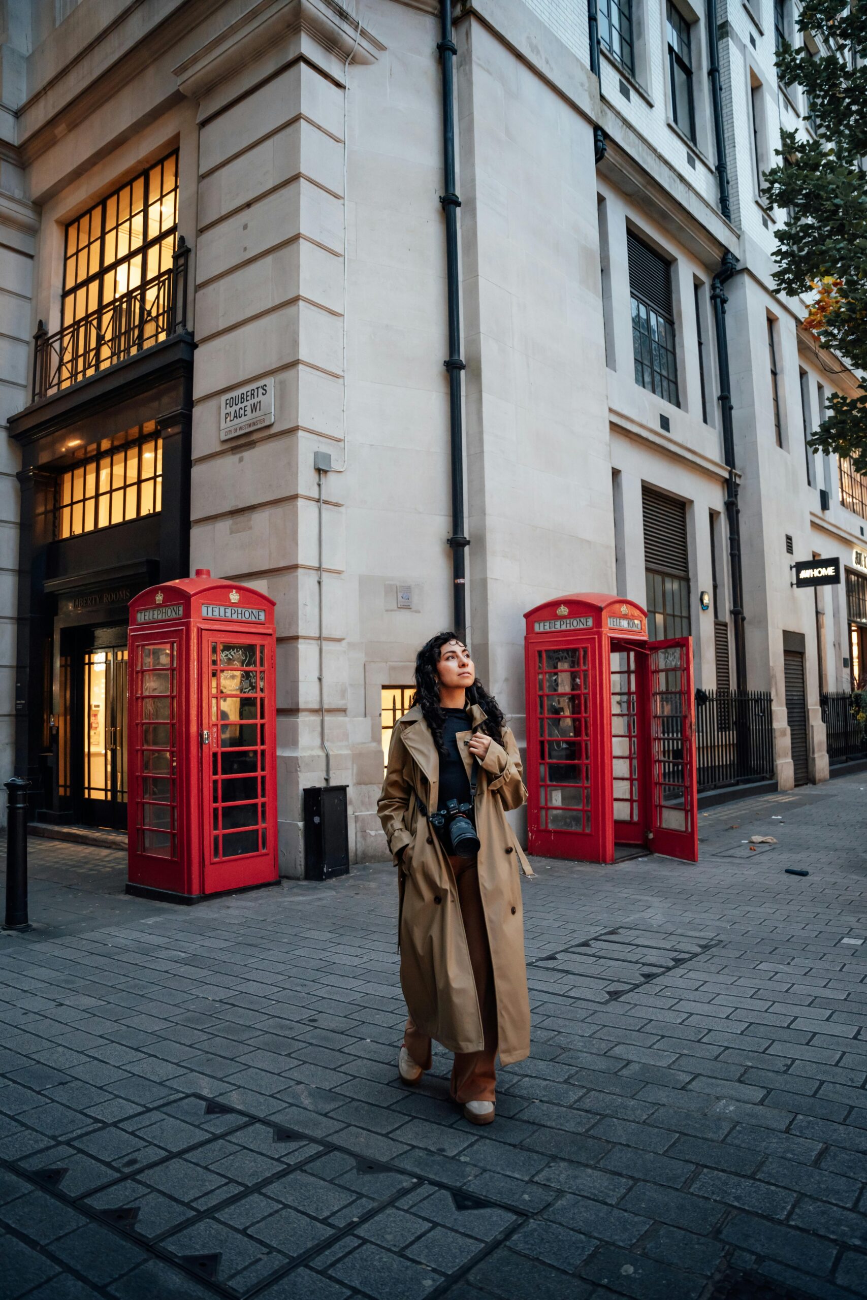 Donna che cammina a Londra con trench beige davanti alle cabine telefoniche rosse, esempio di outfit perfetto per capire come vestirsi a Londra