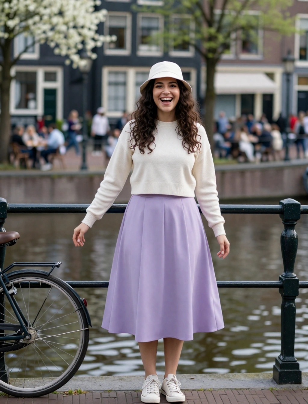 Donna con cappello bucket bianco, maglione crema e gonna lilla passeggia lungo i canali di Amsterdam in primavera.