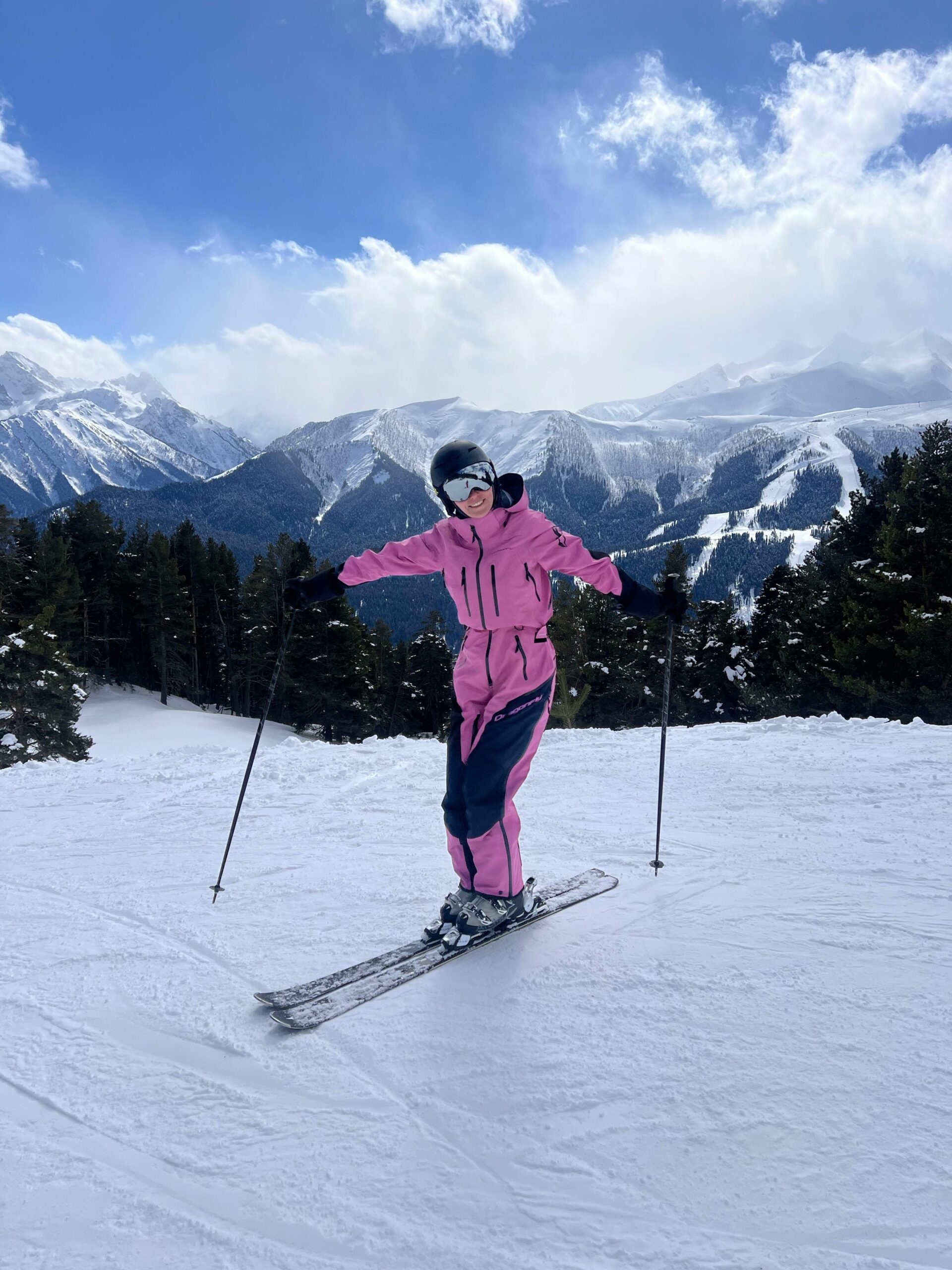 Donna sulle piste da sci con tuta rosa e casco nero, esempio di outfit femminile per sciare in montagna