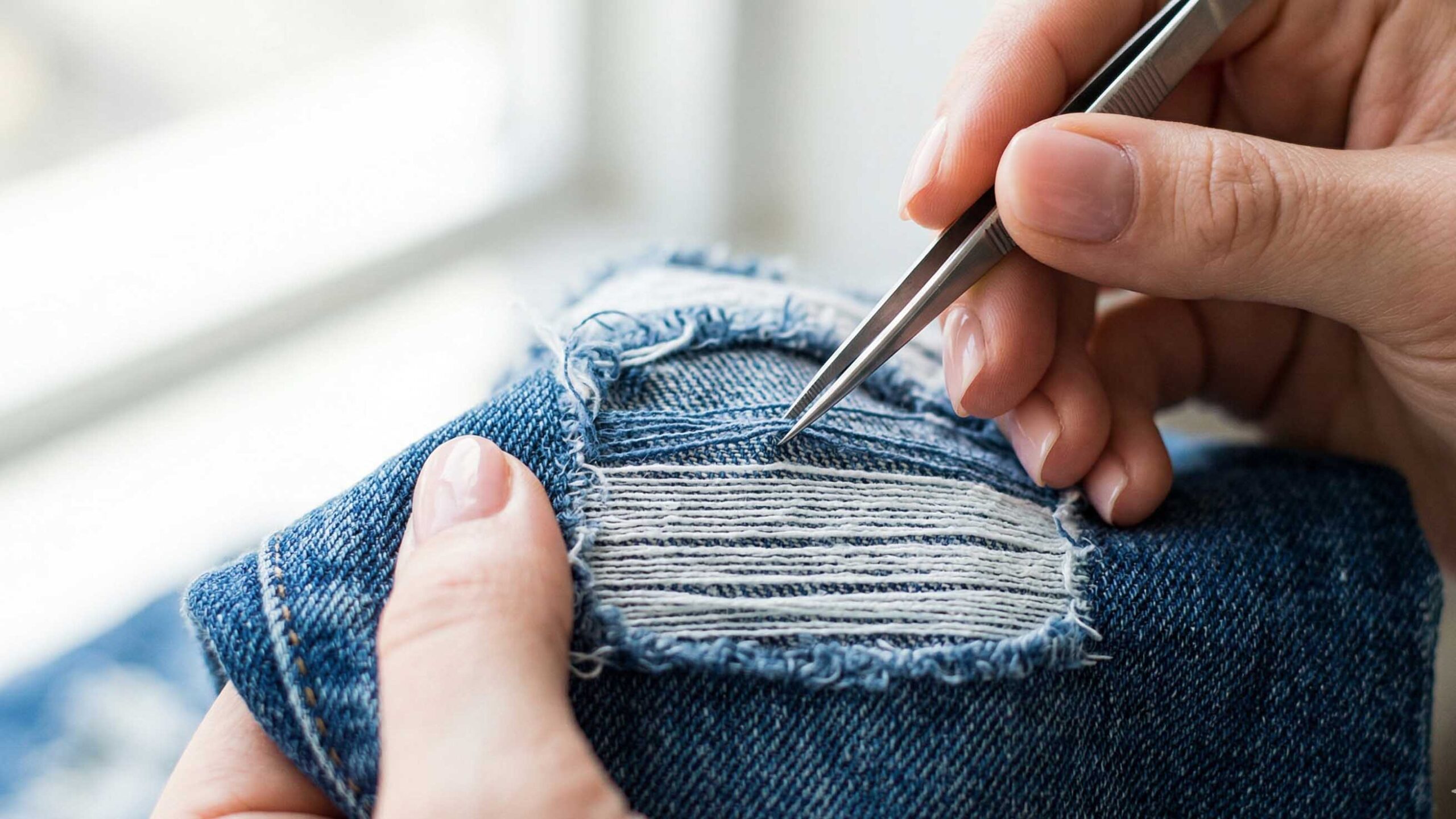 Dettaglio della rimozione dei fili blu per creare l'effetto sfilacciato bianco sui jeans.