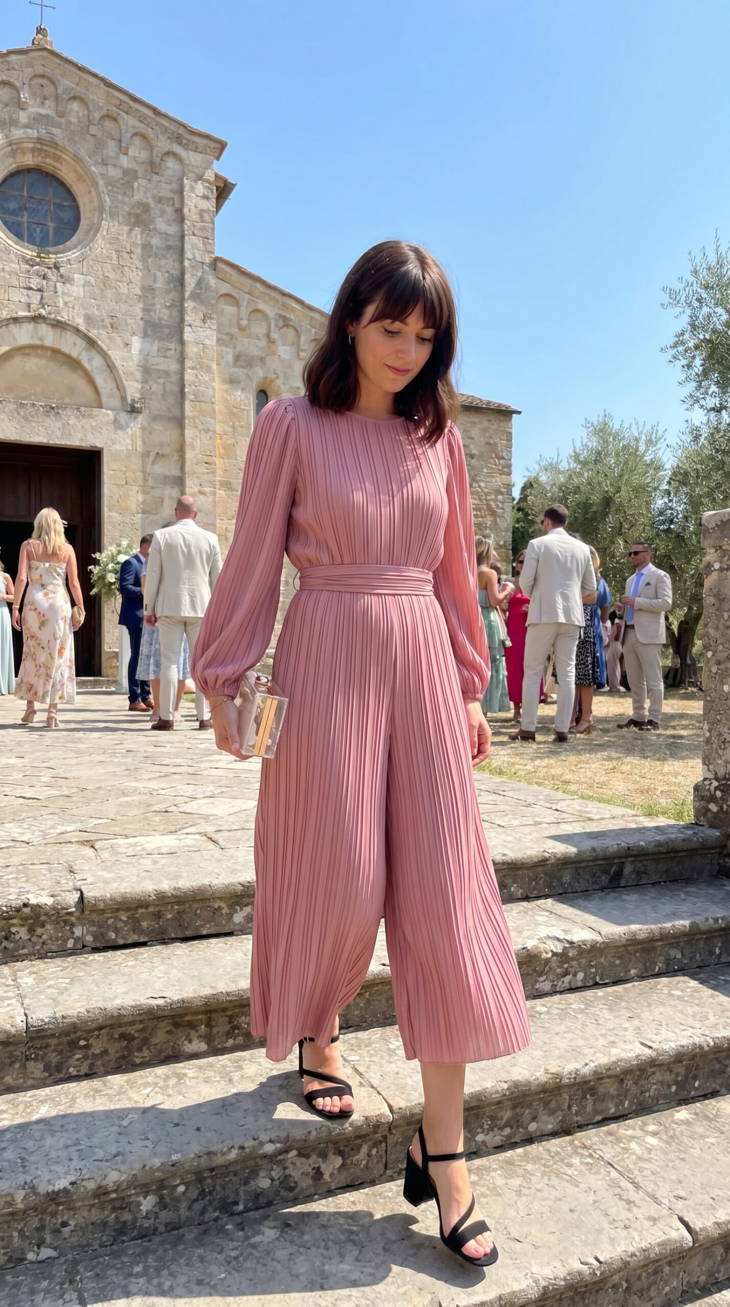 Invitata a un battesimo indossa un'elegante tuta intera plissettata color rosa antico con maniche lunghe.