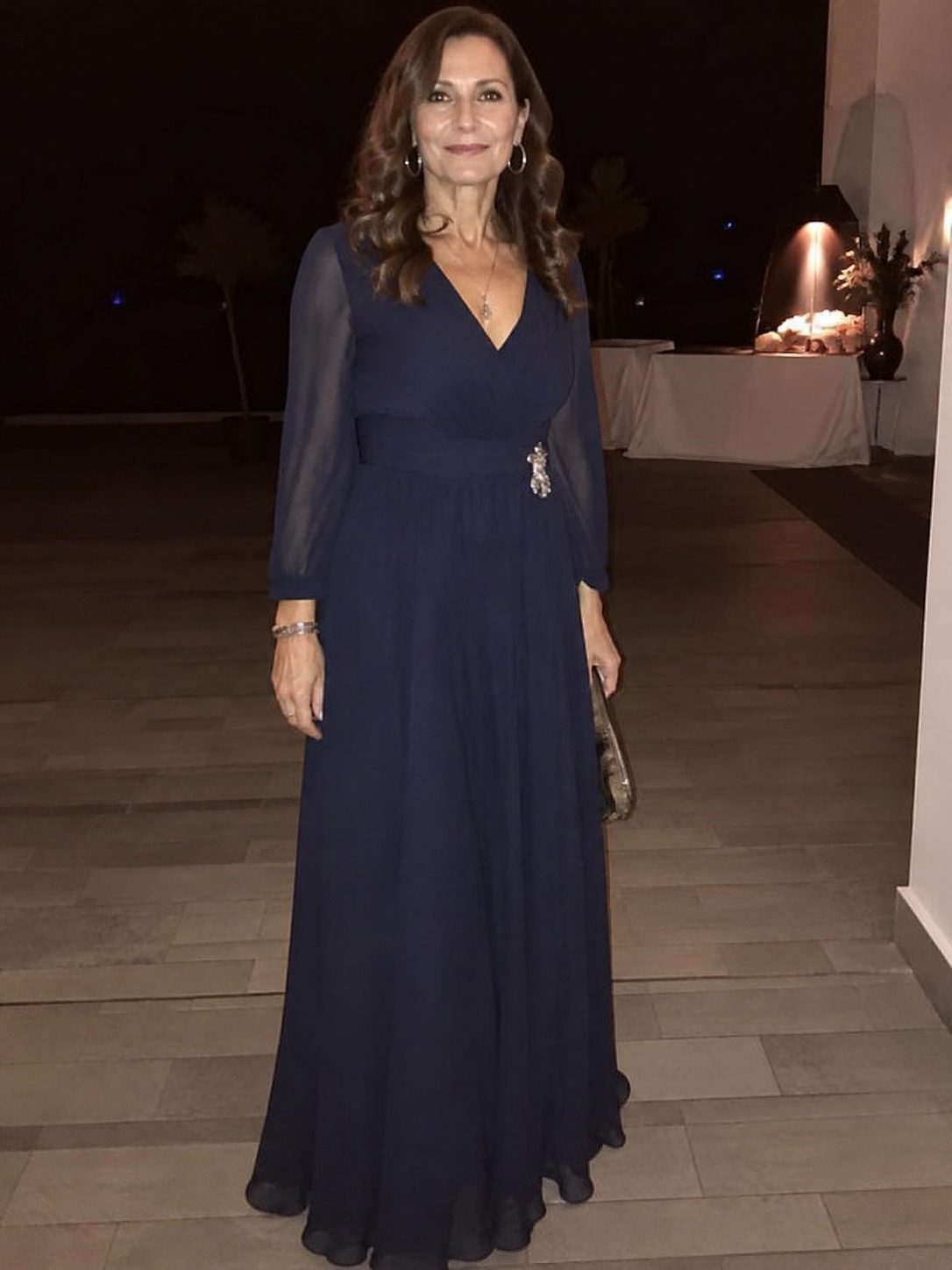 Donna di 60 anni giovanile con abito lungo fluido blu scuro a maniche lunghe durante un evento serale
