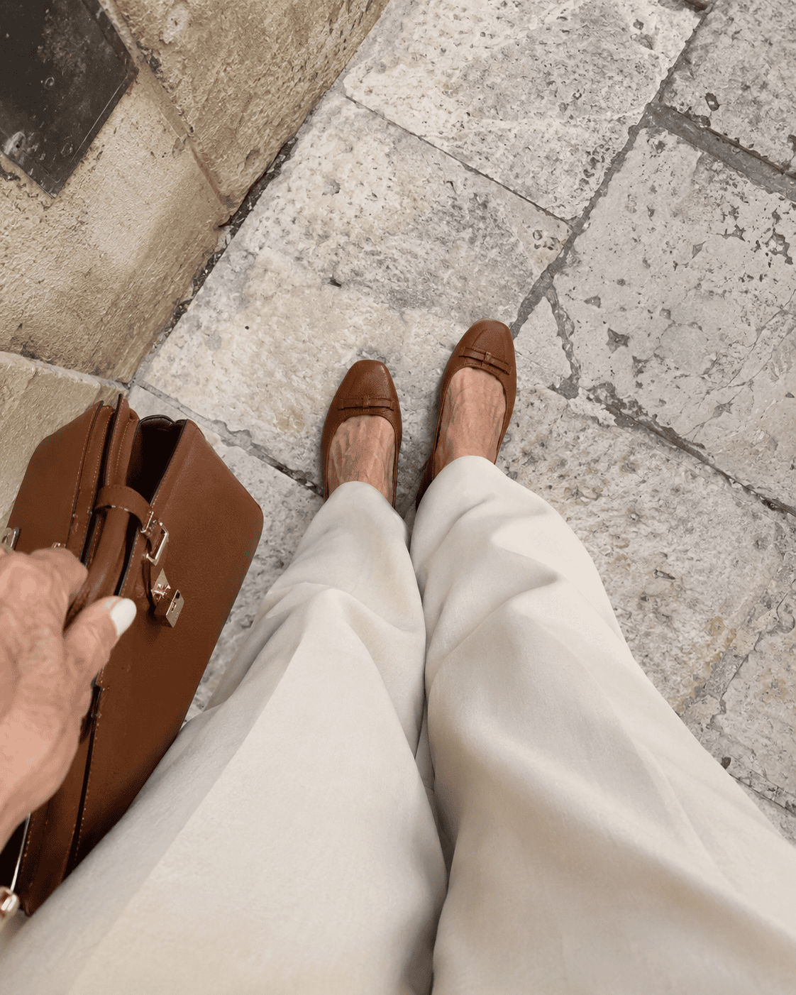 Come Vestirsi a 70 Anni: Guida Completa e Consigli Pratici 21 Dettaglio di ballerine color cognac e pantaloni palazzo crema con borsa in pelle