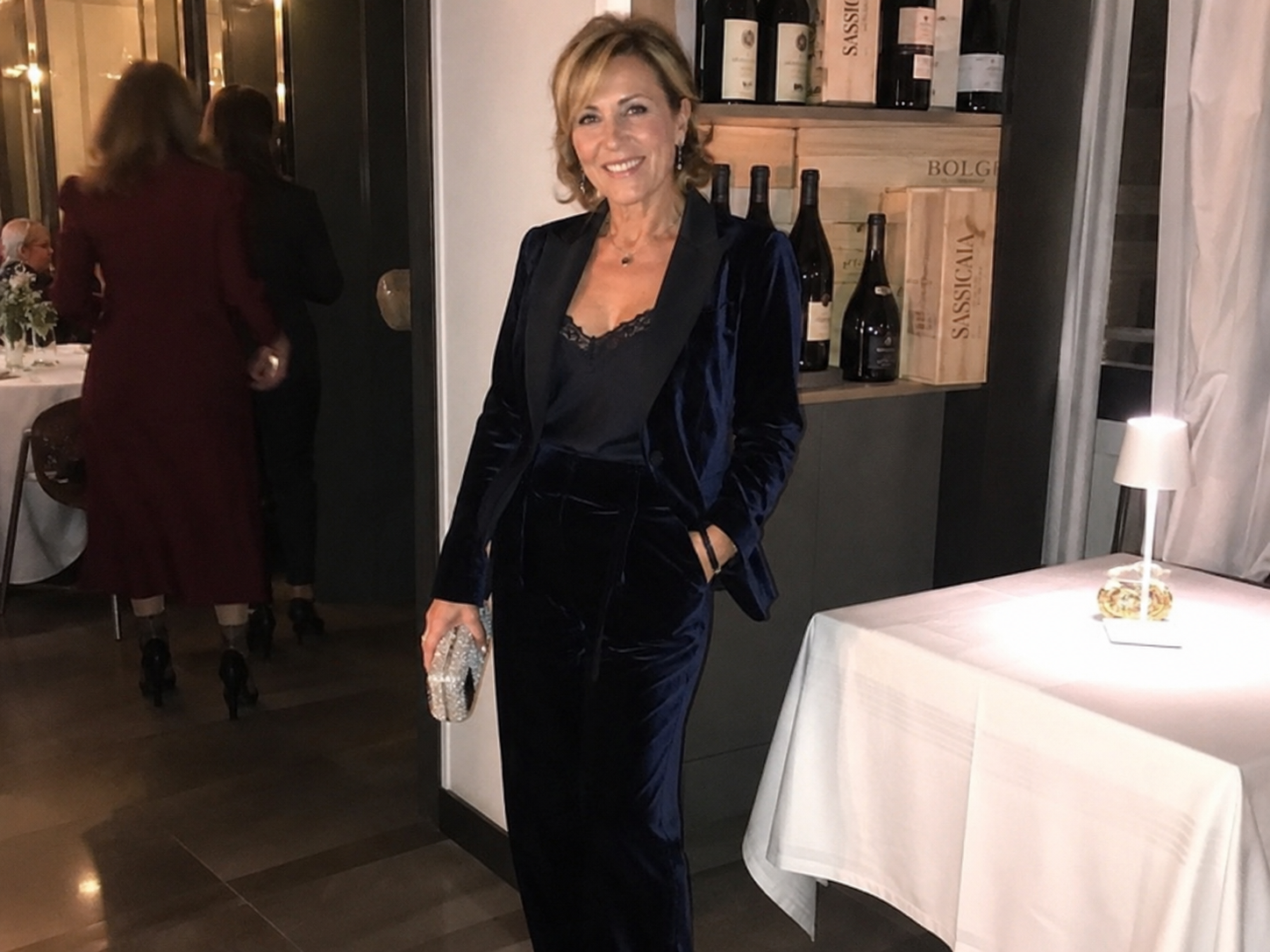 Donna di 60 anni giovanile con completo pantalone in velluto blu notte a una cena al ristorante