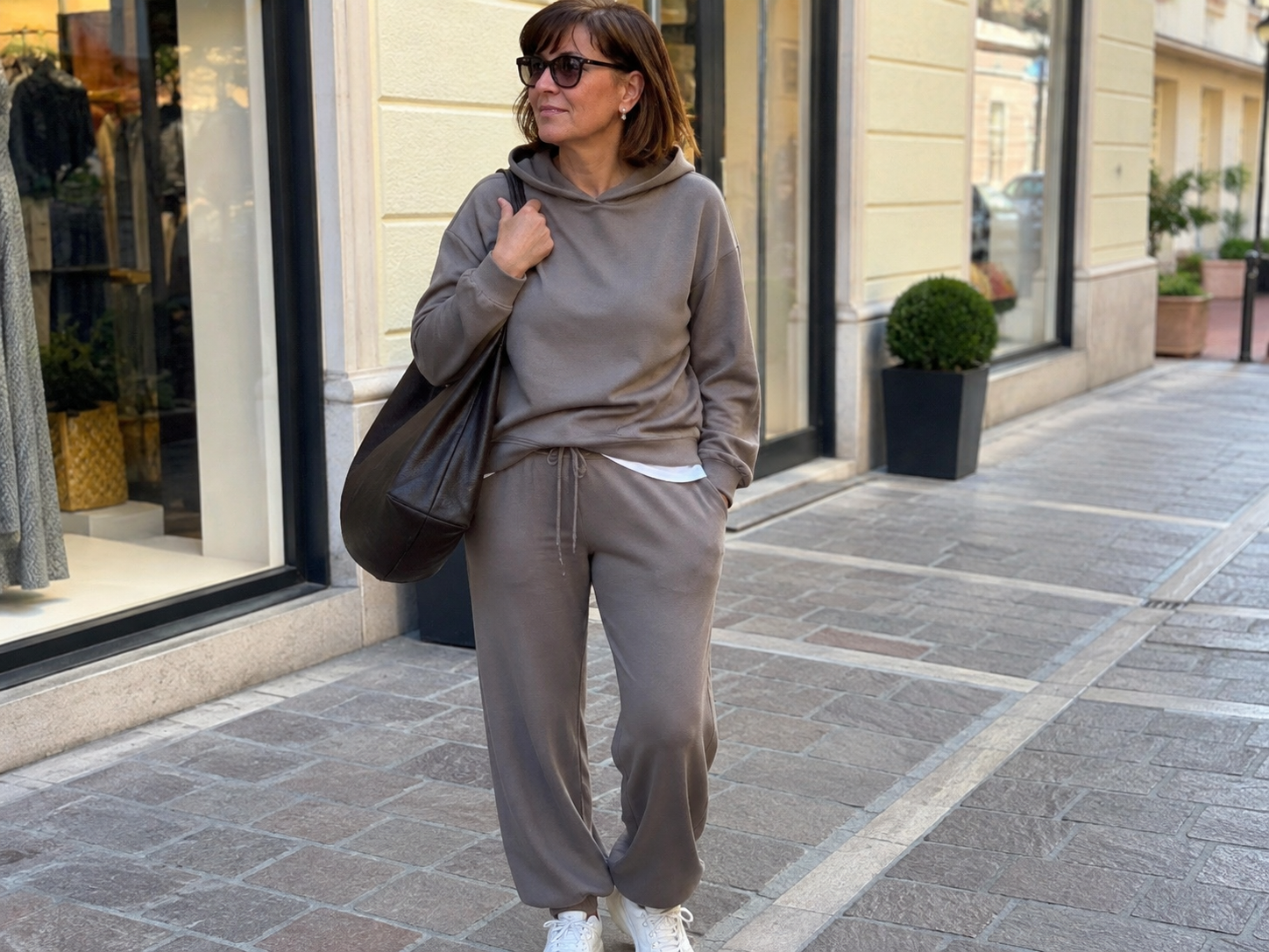Donna di circa 60 anni con tuta elegante in maglia felpata, occhiali da sole e borsa capiente in pelle durante il weekend
