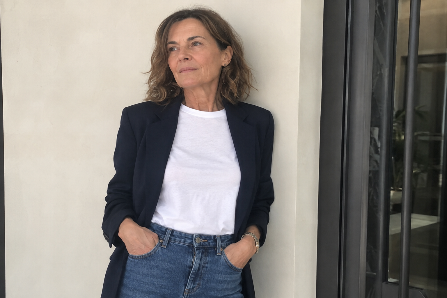 donna di 60 anni che indossa un blazer blu navy, una t-shirt bianca e un jeans a vita alta