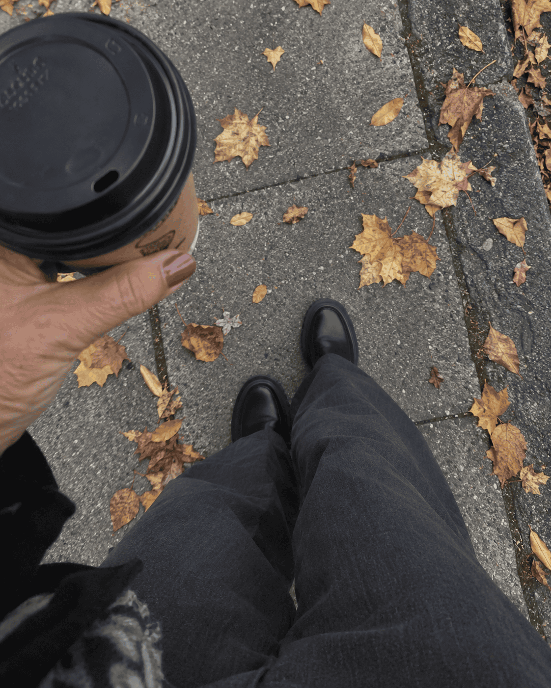 Come Vestirsi a 70 Anni: Guida Completa e Consigli Pratici 22 Dettaglio di pantaloni palazzo grigio scuro e scarpe nere con un caffè da asporto in mano