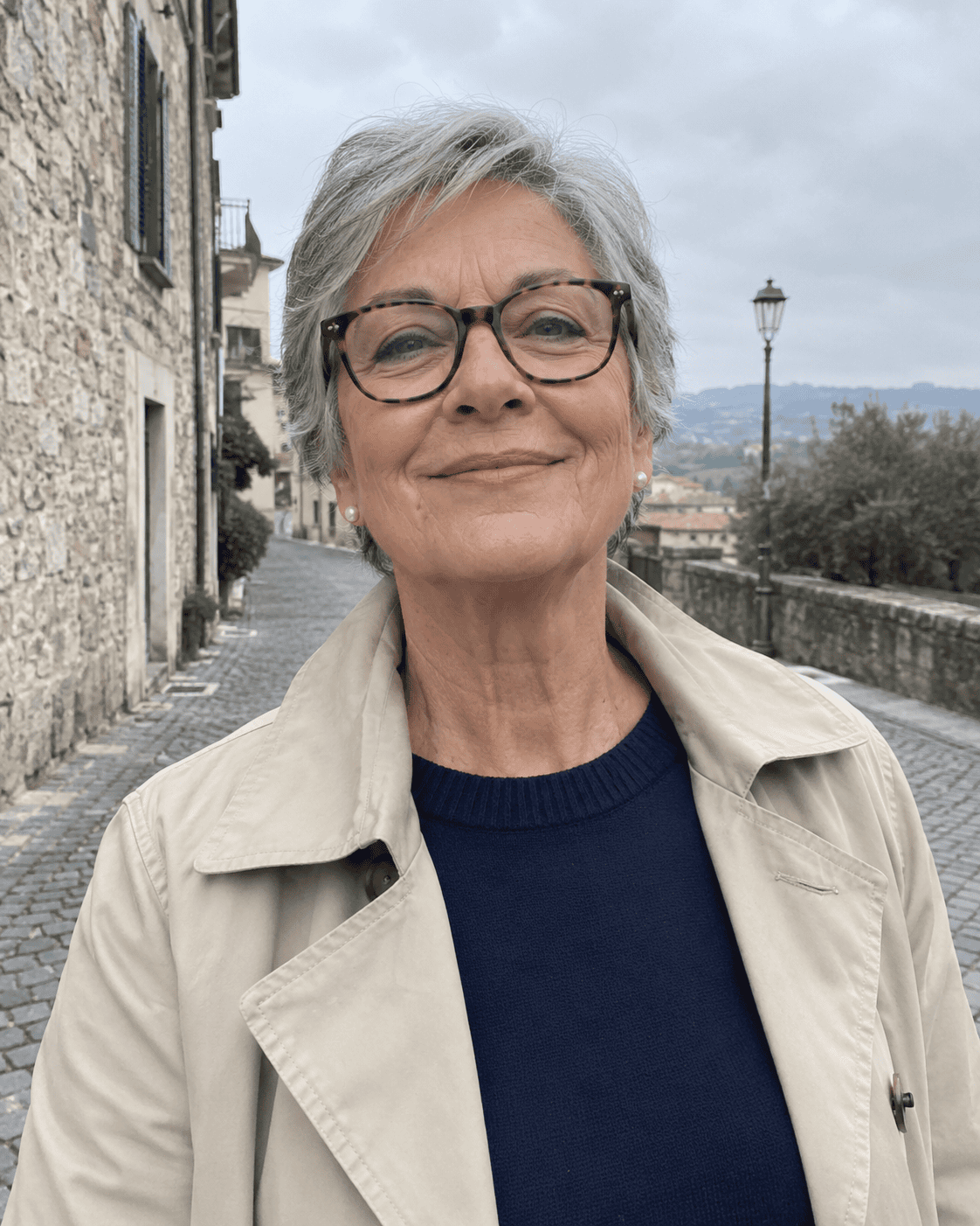 Come Vestirsi a 70 Anni: Guida Completa e Consigli Pratici 2 Donna di 70 anni con trench beige, maglione blu notte e occhiali da vista in un centro storico