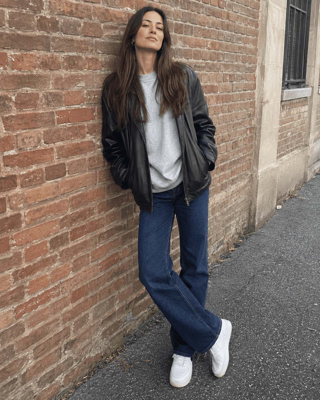 Outfit weekend 12 gradi: jeans dritti blu, felpa grigia, giacca in pelle nera e sneakers bianche
