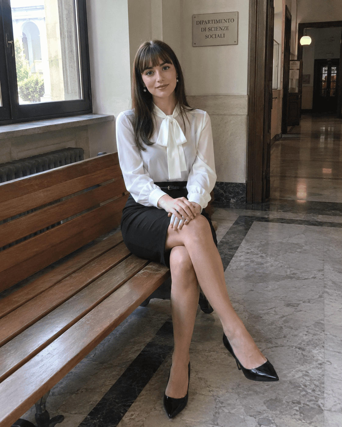 Laureanda seduta su una panca con gonna a tubino nera, blusa bianca con fiocco, cintura sottile e scarpe nere a punta, outfit laurea elegante